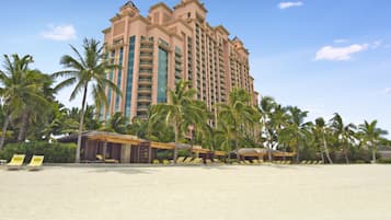 Un hotel frente al mar con varios pisos, palmeras y una playa de arena.