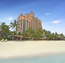 Un hotel frente al mar con varios pisos, palmeras y una playa de arena.