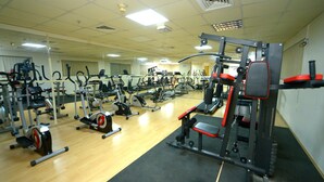 A gym with various exercise machines, a mirrored wall, and a wooden floor. - Nejoum Al Emarate (Sharjah)