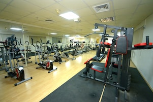 Un gimnasio con diferentes máquinas de ejercicio, un espejo grande y suelo de madera.
