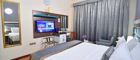 A hotel room with a large bed, a desk with a computer, a TV, and a clock on the wall.