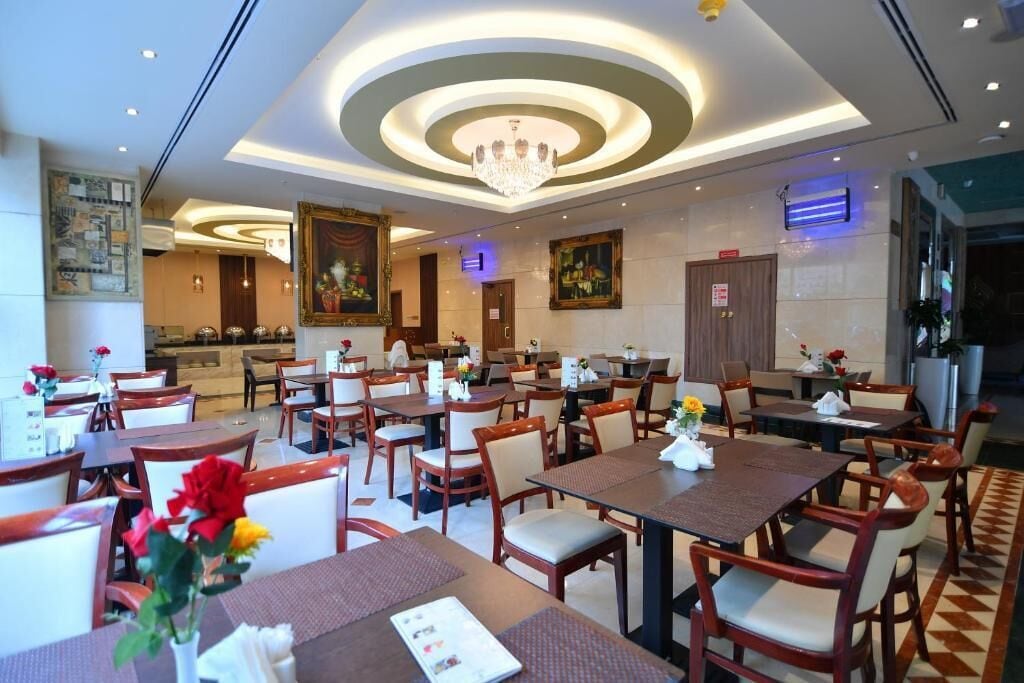 A hotel dining area with multiple tables and chairs, a chandelier, and framed artwork on the walls.