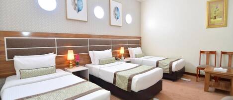 Een hotelkamer met drie bedden, een houten hoofdbord, een tafeltje en een stoel.