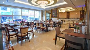 A spacious restaurant with multiple dining tables and chairs, large windows offering a view of the street, and a chandelier on the ceiling. - Nejoum Al Emarate (Sharjah)