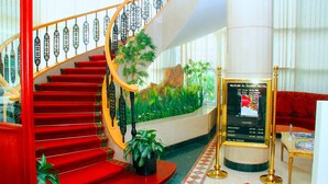 A grand staircase with red steps and a glass railing, leading to a lobby area with a large potted plant and a signboard displaying hotel information. - Nejoum Al Emarate (Sharjah)