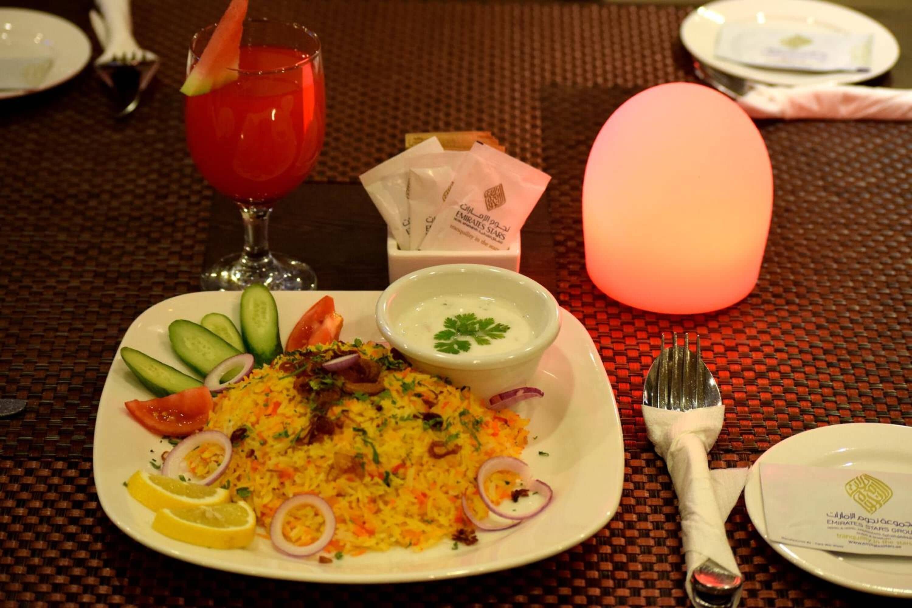 A meal with rice, vegetables, and a side of soup, accompanied by a glass of red drink and a lit candle on a table.