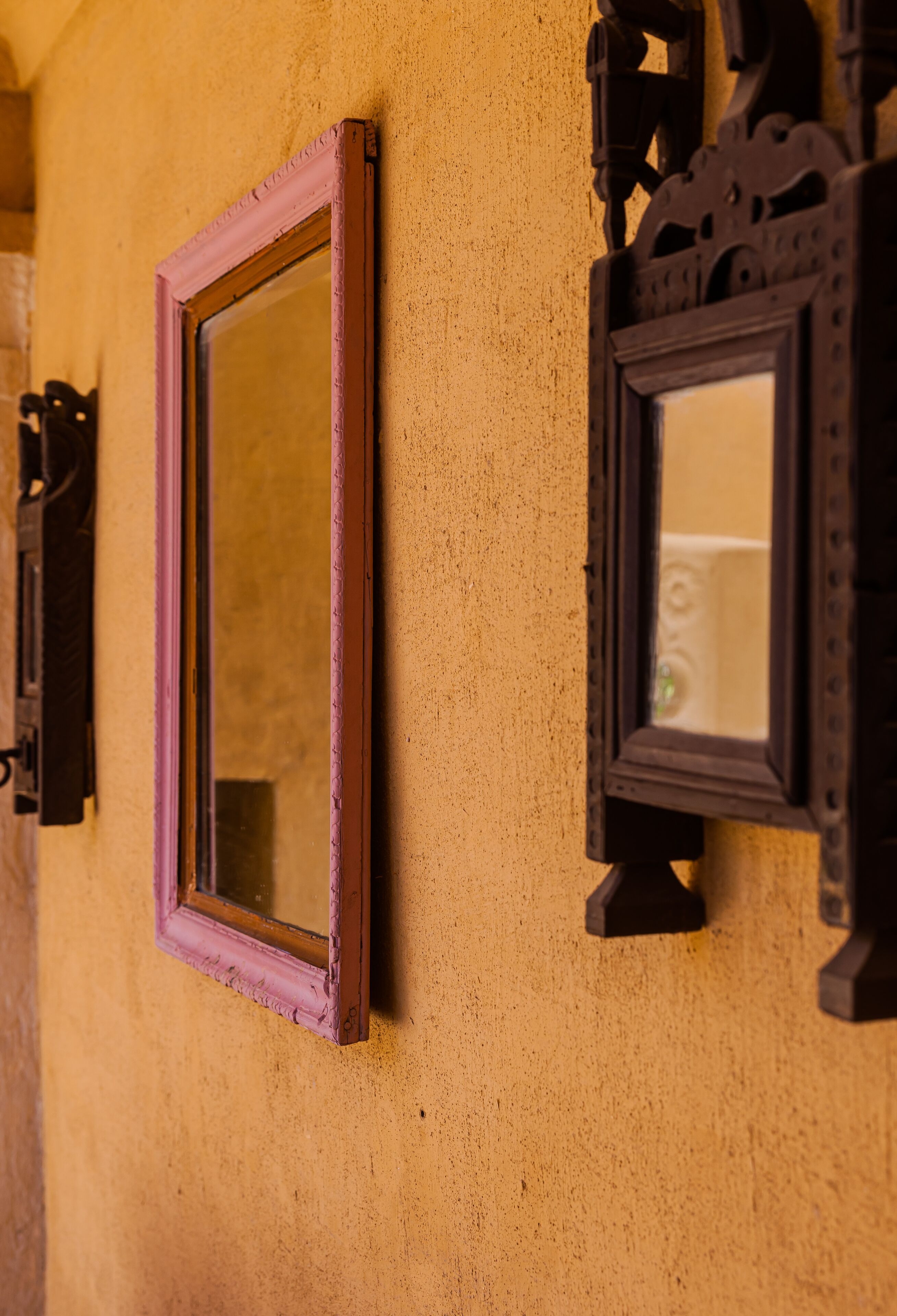 Two wall-mounted mirrors with ornate frames against a textured wall.