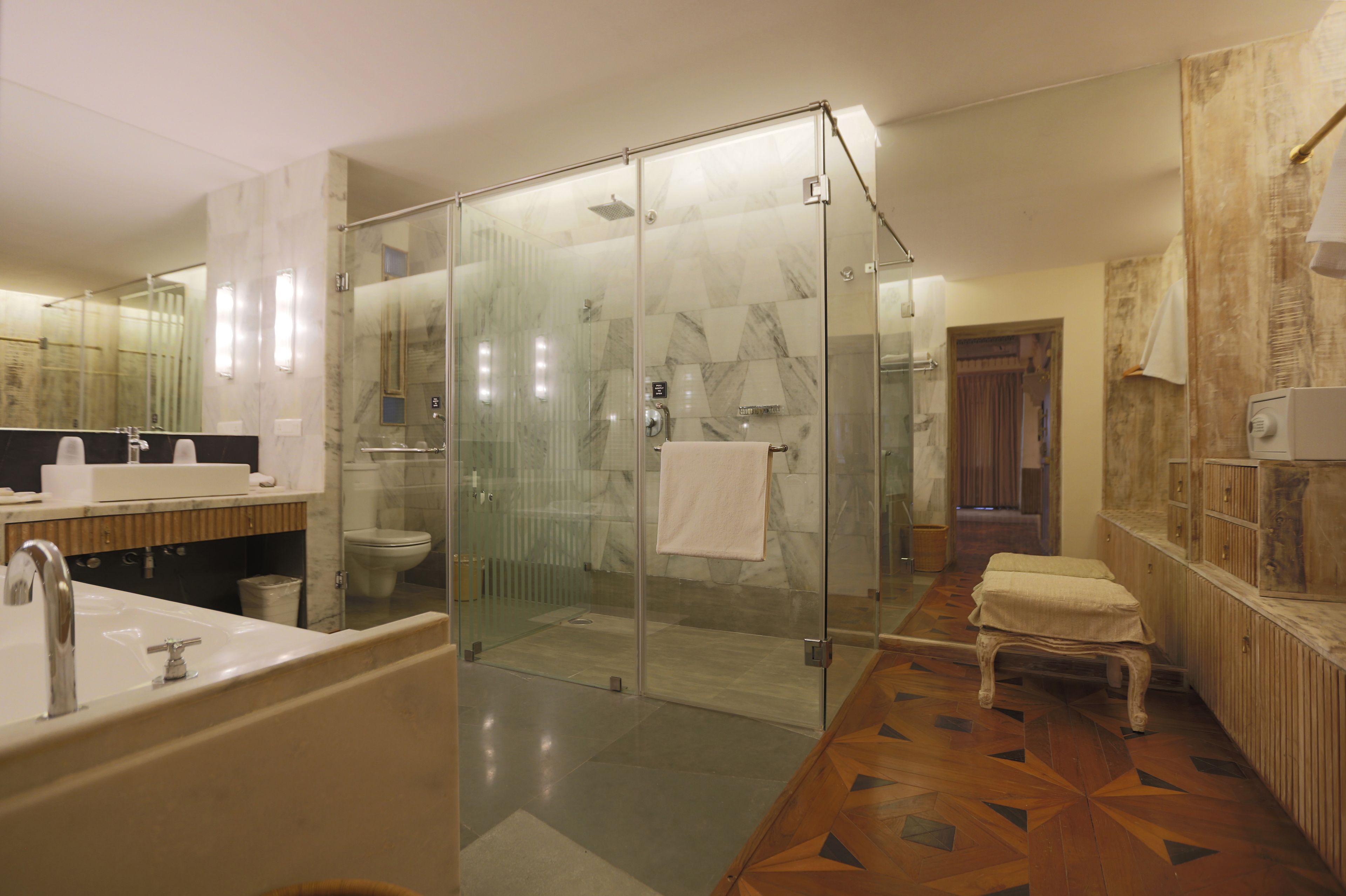 Een moderne badkamer met een douchecabine van glas, een grote spiegel, een badkuip en een houten vloerpatroon.