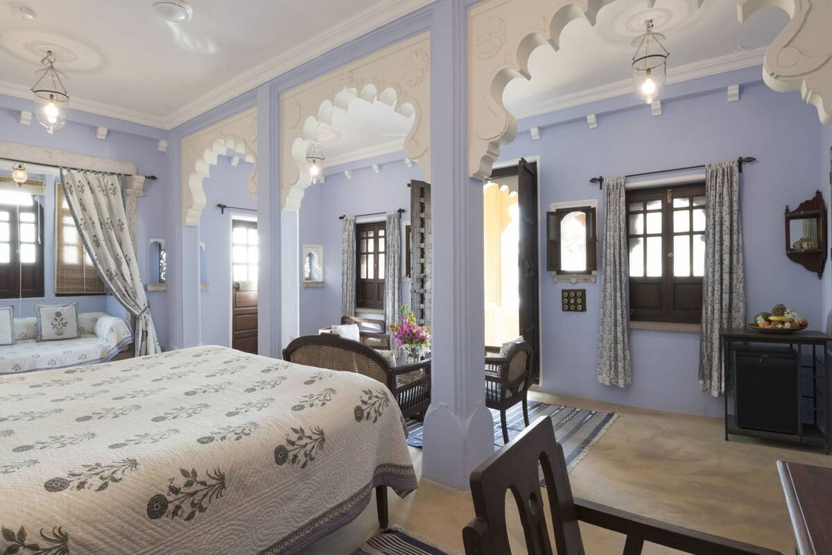 A room with a bed, a desk, a chair, a lamp, and a small table with a decorative item.