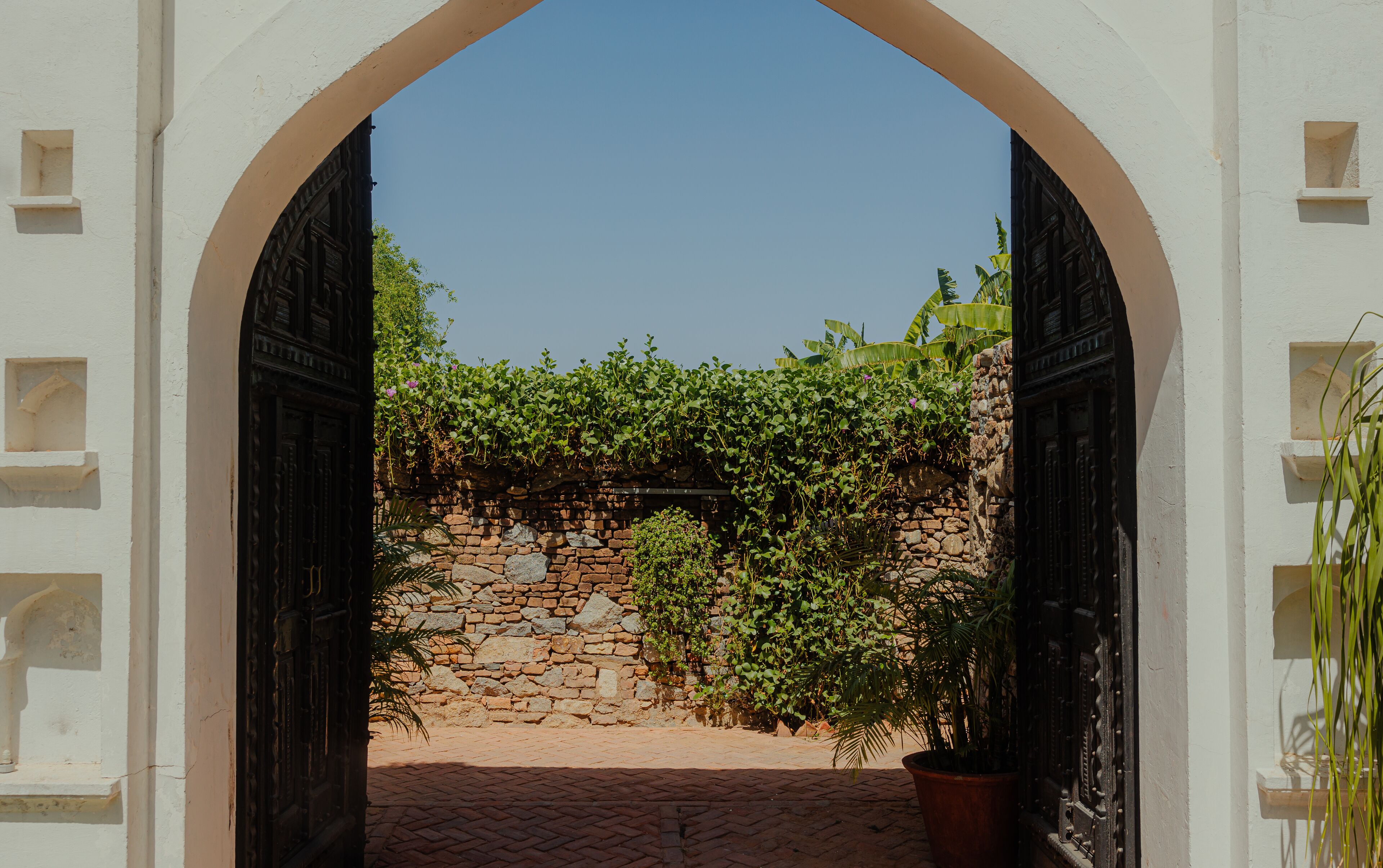 An arched doorway leading to a courtyard with a stone wall and potted plants.