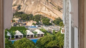 A view through an arched window of a resort with a pool, greenery, and a mountainous backdrop. - Rawla Narlai (Desuri)