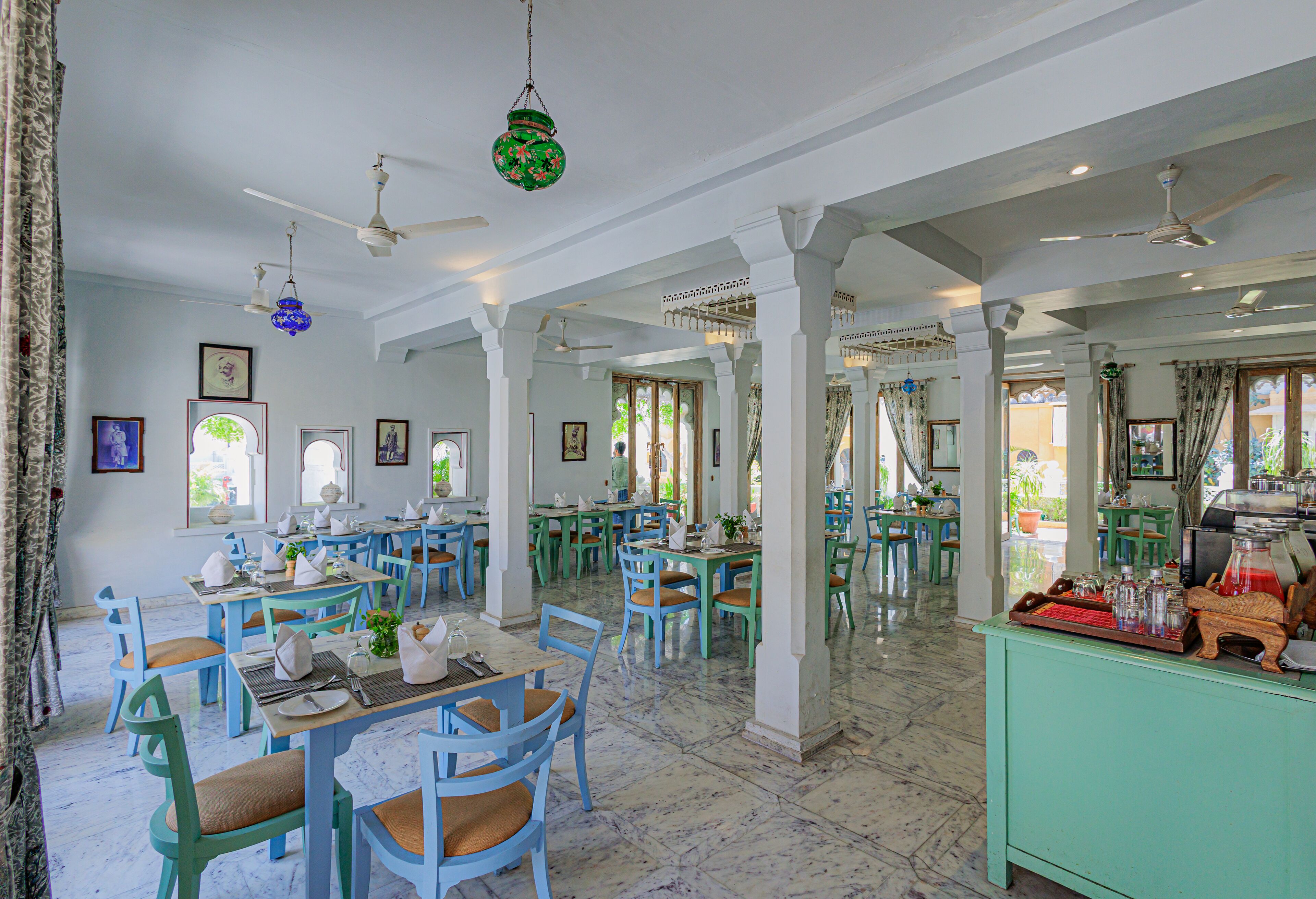 Un comedor amplio con varias mesas y sillas, ventiladores de techo y una zona de bar verde.