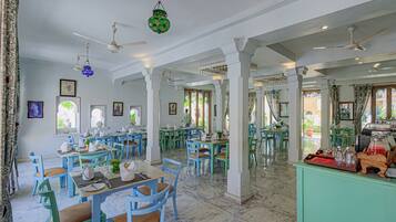 Un comedor amplio con varias mesas y sillas, ventiladores de techo y una zona de bar verde.