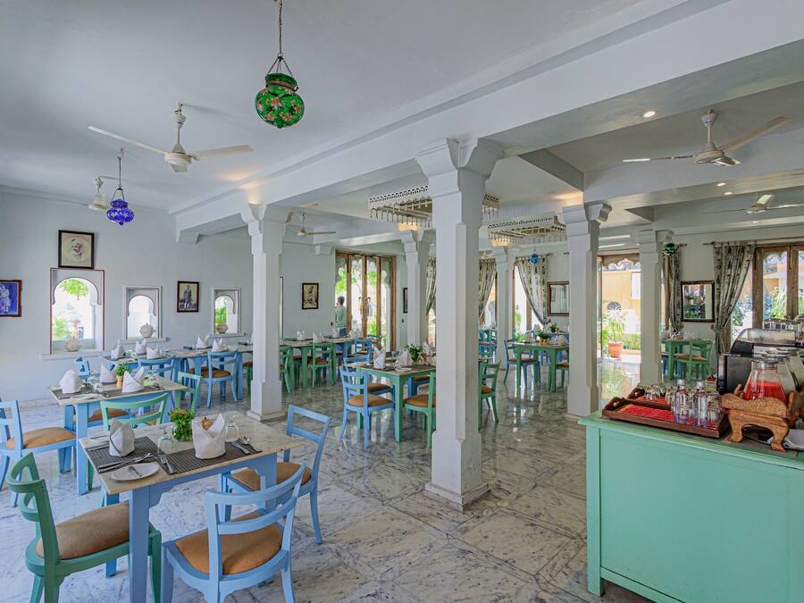 Un comedor amplio con varias mesas y sillas, ventiladores de techo y una zona de bar verde.