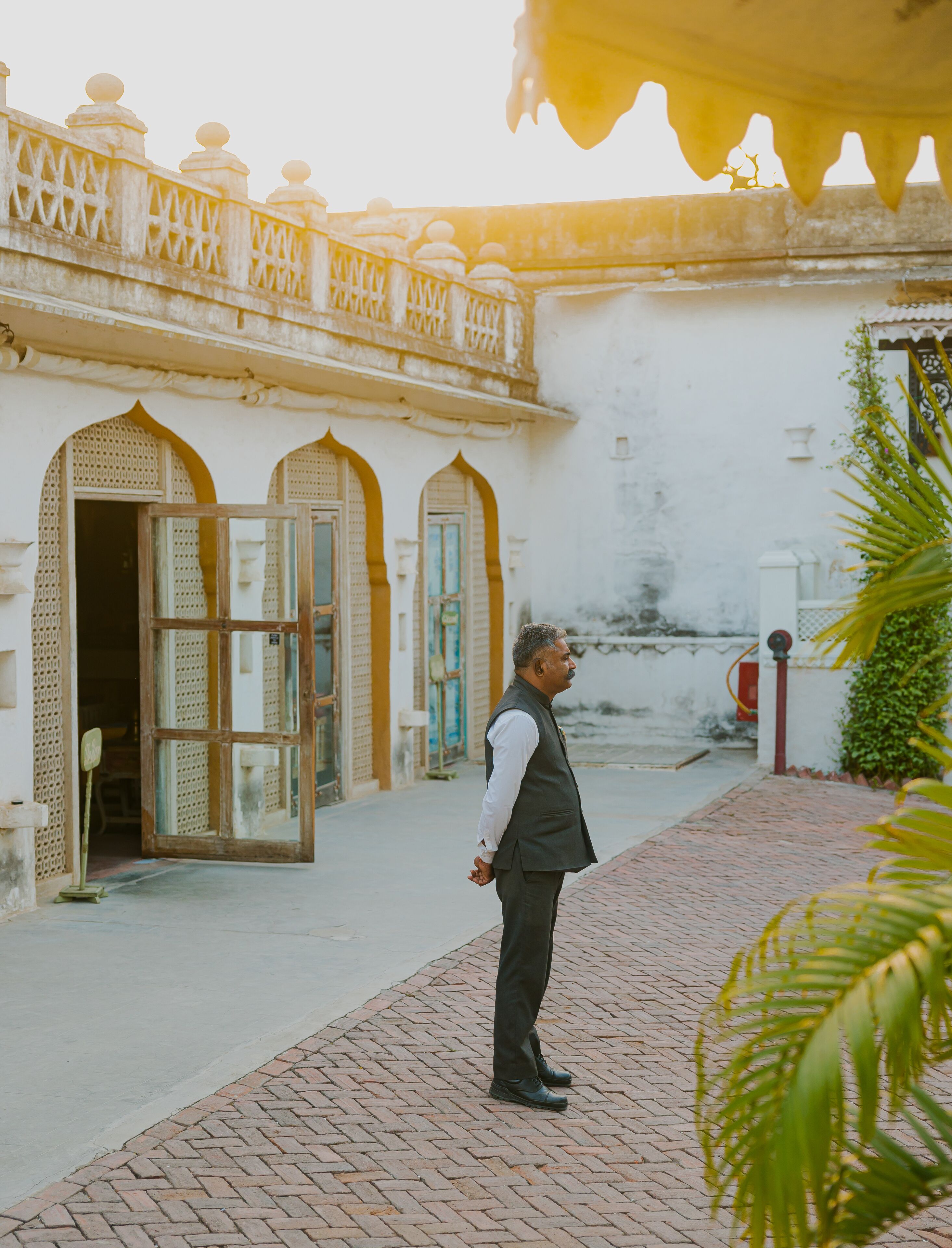A man standing in a courtyard with traditional architecture, including arched doorways and a decorative railing.