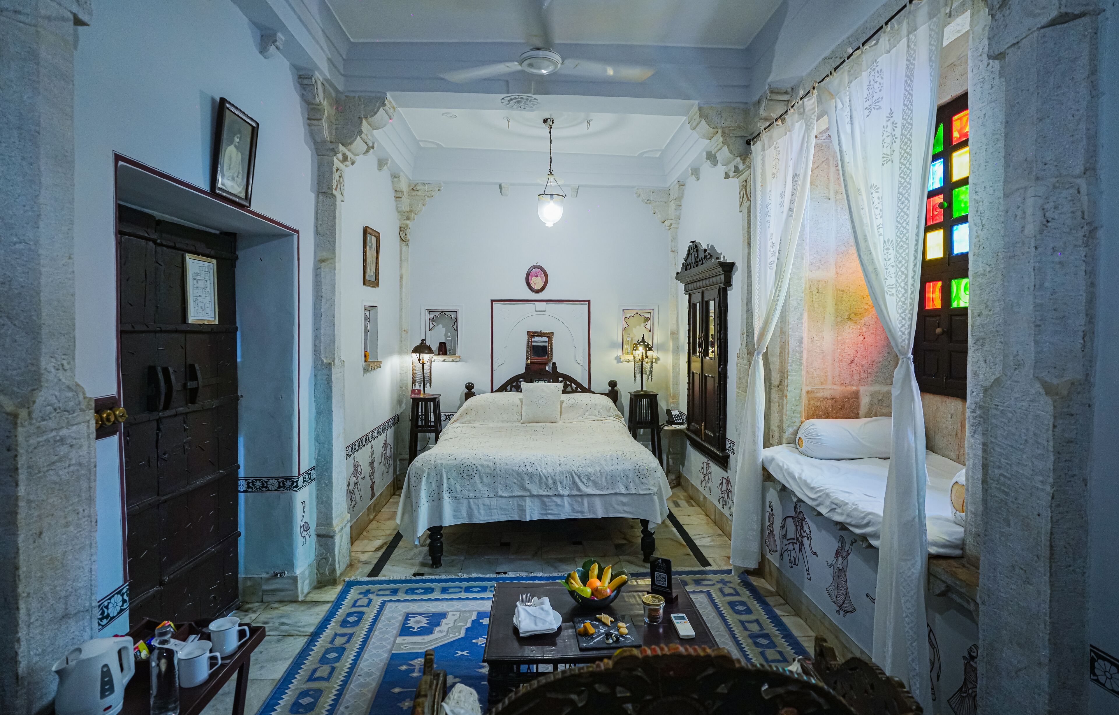 A traditional room with a bed, a desk, and a small table with a bowl of fruit.