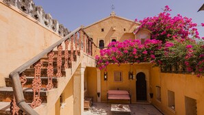 A courtyard with a staircase, a bed, and a building with pink flowers. - Rawla Narlai (Desuri)