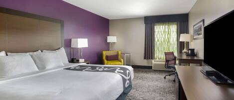 A hotel room with a large bed, a desk, a chair, and a television.