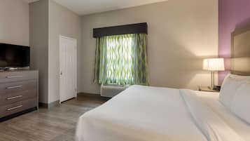 A hotel room with a bed, a TV, a dresser, a door, and a window with curtains.