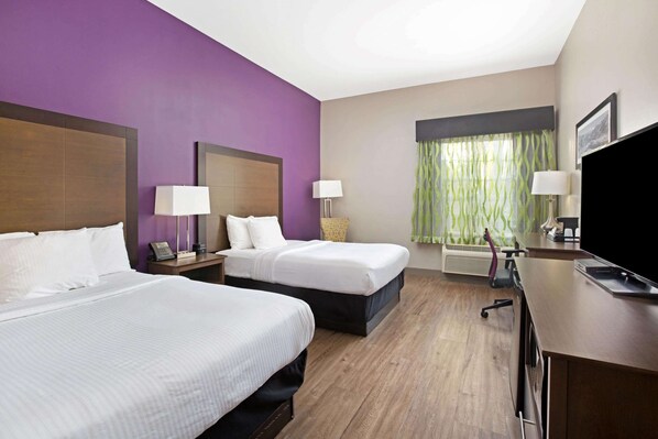 Habitación de hotel con dos camas, un escritorio, un televisor y una ventana con cortinas.