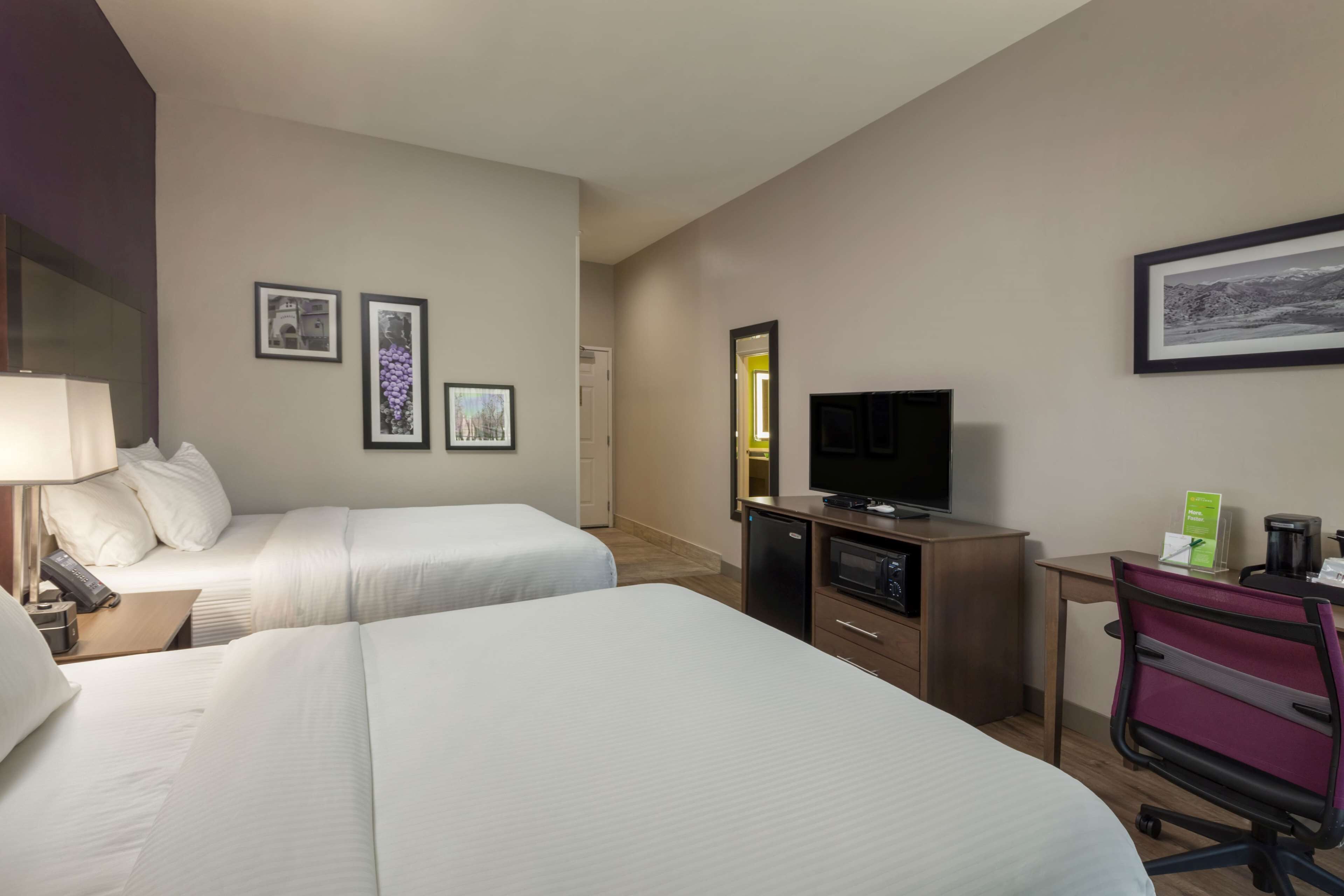 Habitación de hotel con dos camas, un escritorio con televisor, cafetera y cuadros en la pared.