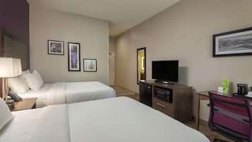 A hotel room with two beds, a desk with a television, a coffee maker, and framed pictures on the wall.
