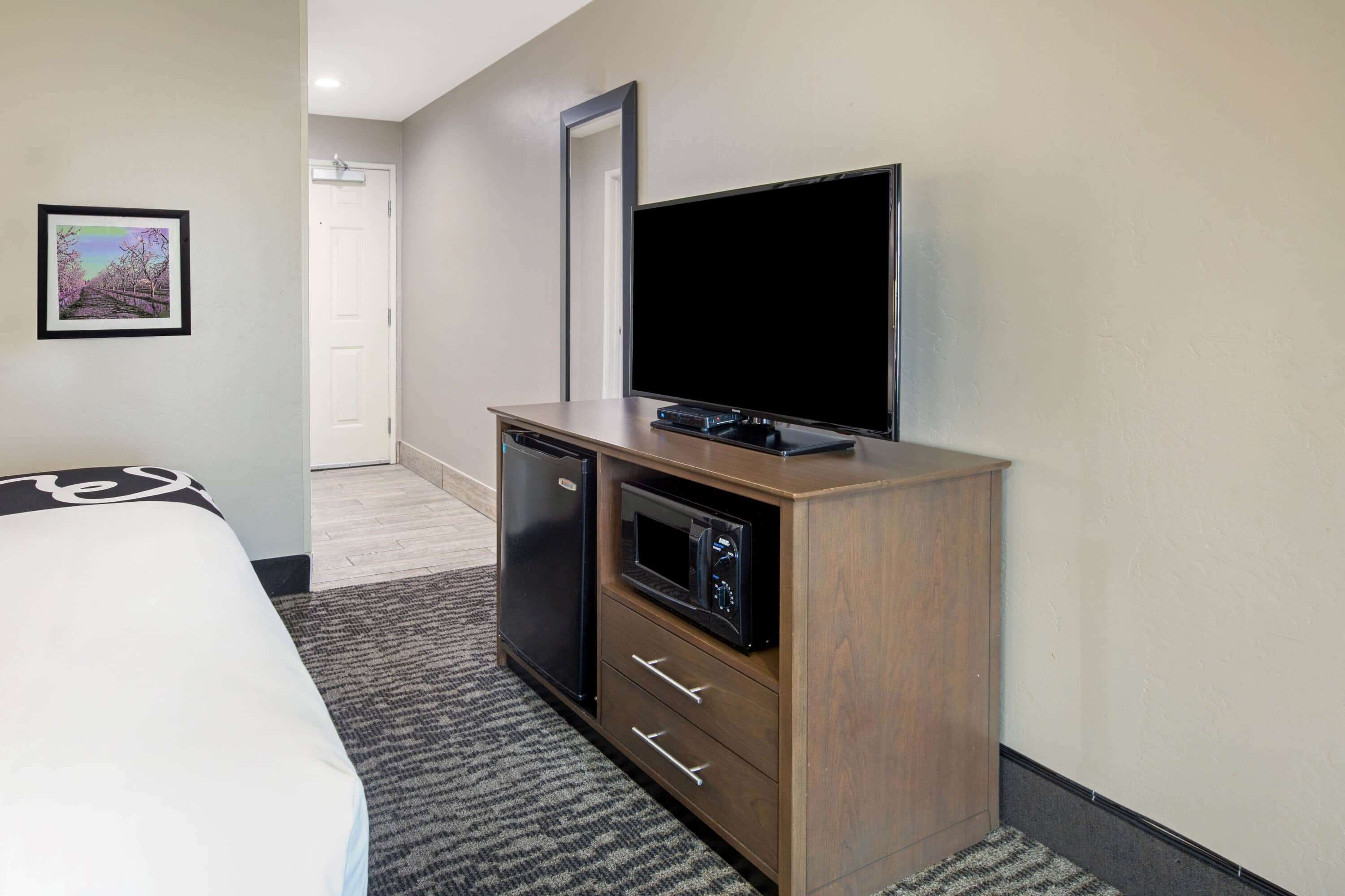 A hotel room with a bed, a wooden cabinet with a flat-screen TV, a microwave, and a refrigerator.
