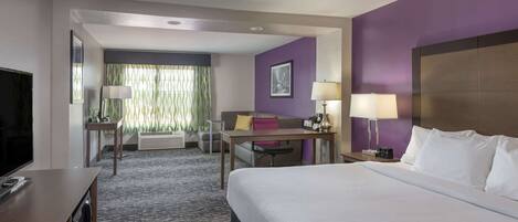 A hotel room with a large bed, a desk with a chair, a television, and a window with curtains.