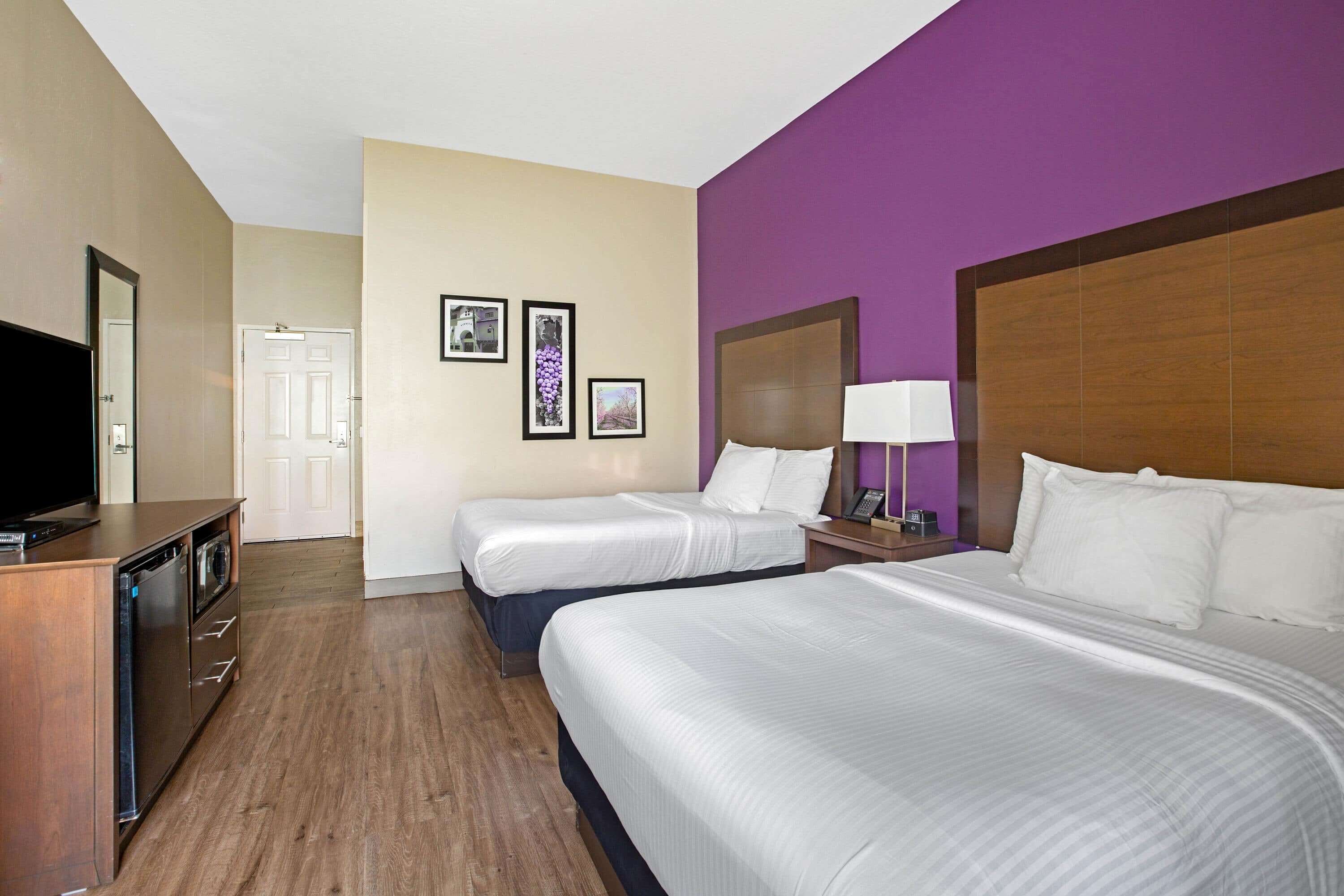 A hotel room with two beds, a TV, a desk, and a bathroom.