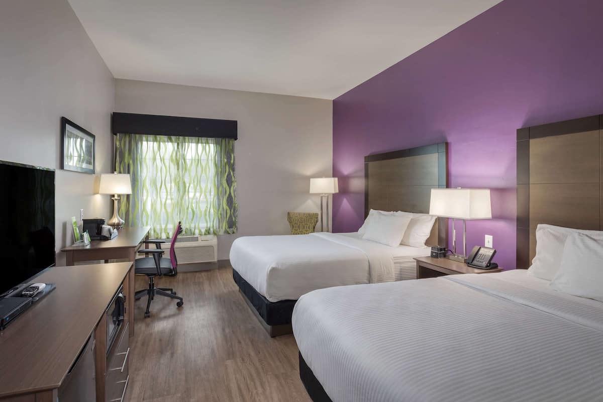 Habitació d'hotel amb dos llits, escriptori amb un ordinador, una cadira, televisió i finestra amb cortines.