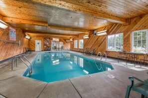Una piscina interior con paredes y techo de madera, rodeada de sillas y mesas.