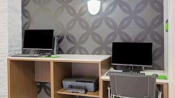 A workspace with two computer desks, each with a monitor, keyboard, and mouse. There are two printers on the desks, and a chair is positioned in front of the desks.