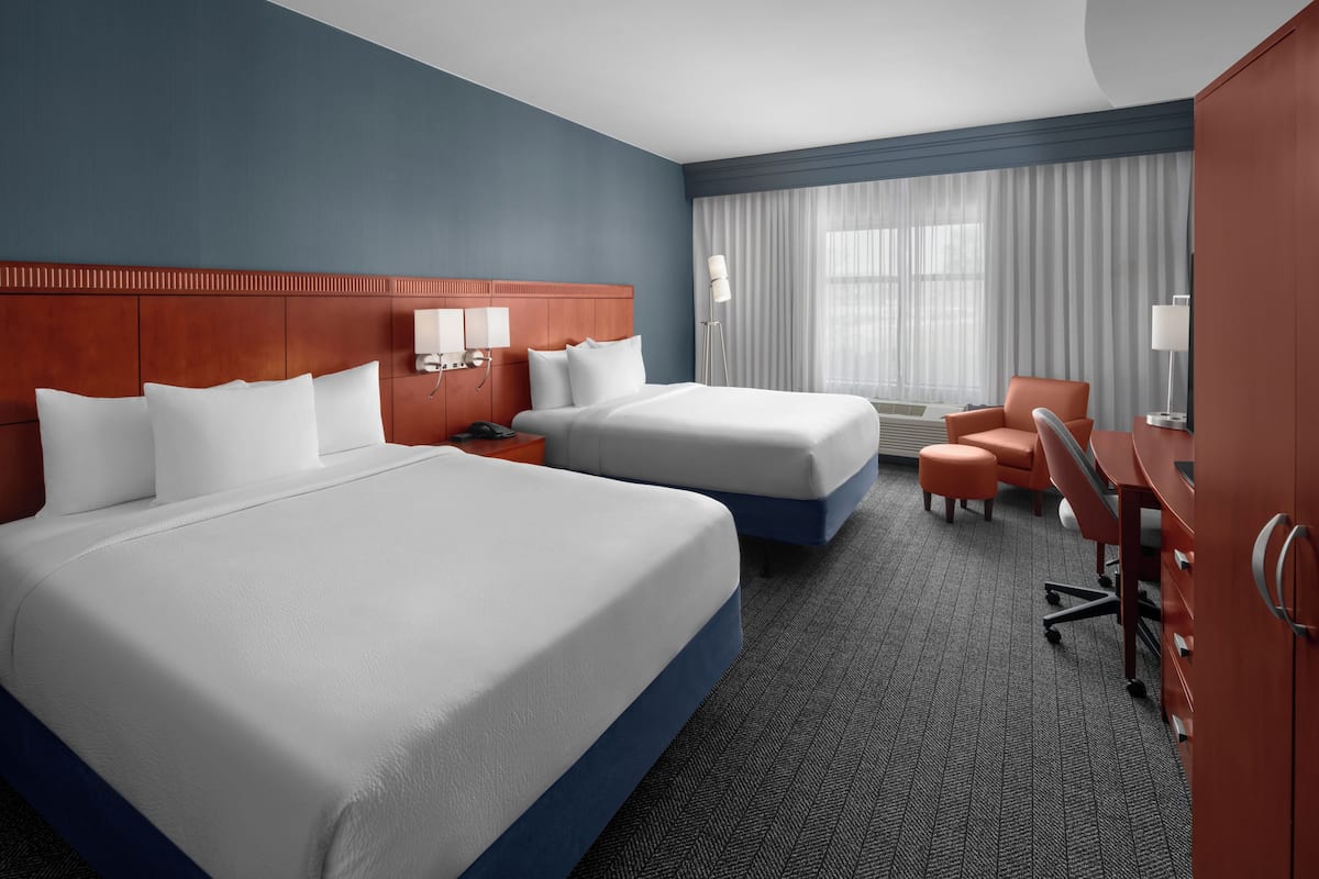 Hotelkamer met twee bedden, een bureau, een stoel, een bureaulamp en een raam met gordijnen.