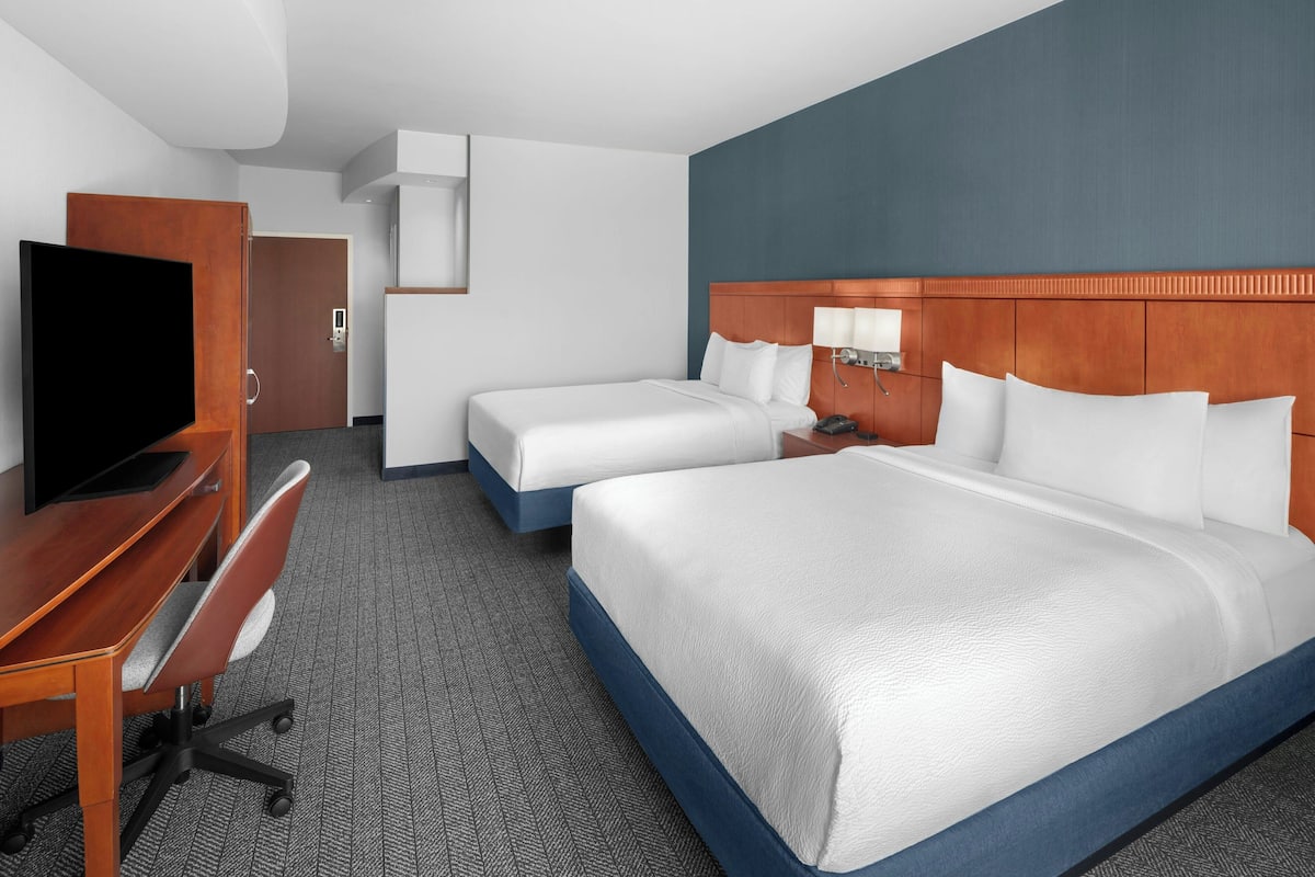 A hotel room with a large bed, a smaller bed, a desk with a chair, a television, and a wardrobe.