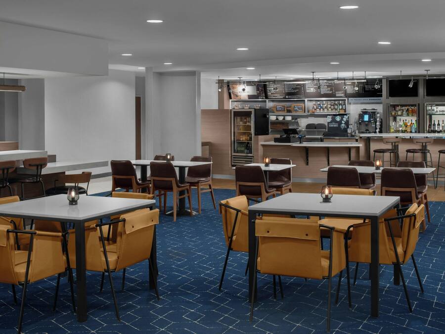 A modern restaurant with multiple tables and chairs, a bar area, and a kitchen in the background.