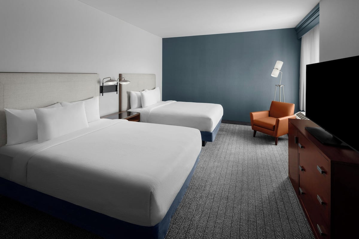 Een hotelkamer met twee bedden, een bureau, een stoel, een televisie en een lamp.