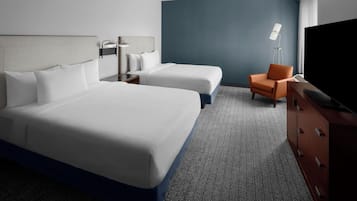 Habitación de hotel con dos camas, un escritorio, una silla, un televisor y una lámpara.