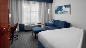 A hotel room with a bed, a desk, a chair, a sofa, and a standing lamp.