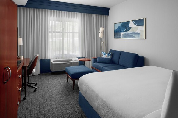 Une chambre d’hôtel comprenant un lit, un bureau, une chaise, un canapé et un lampadaire.