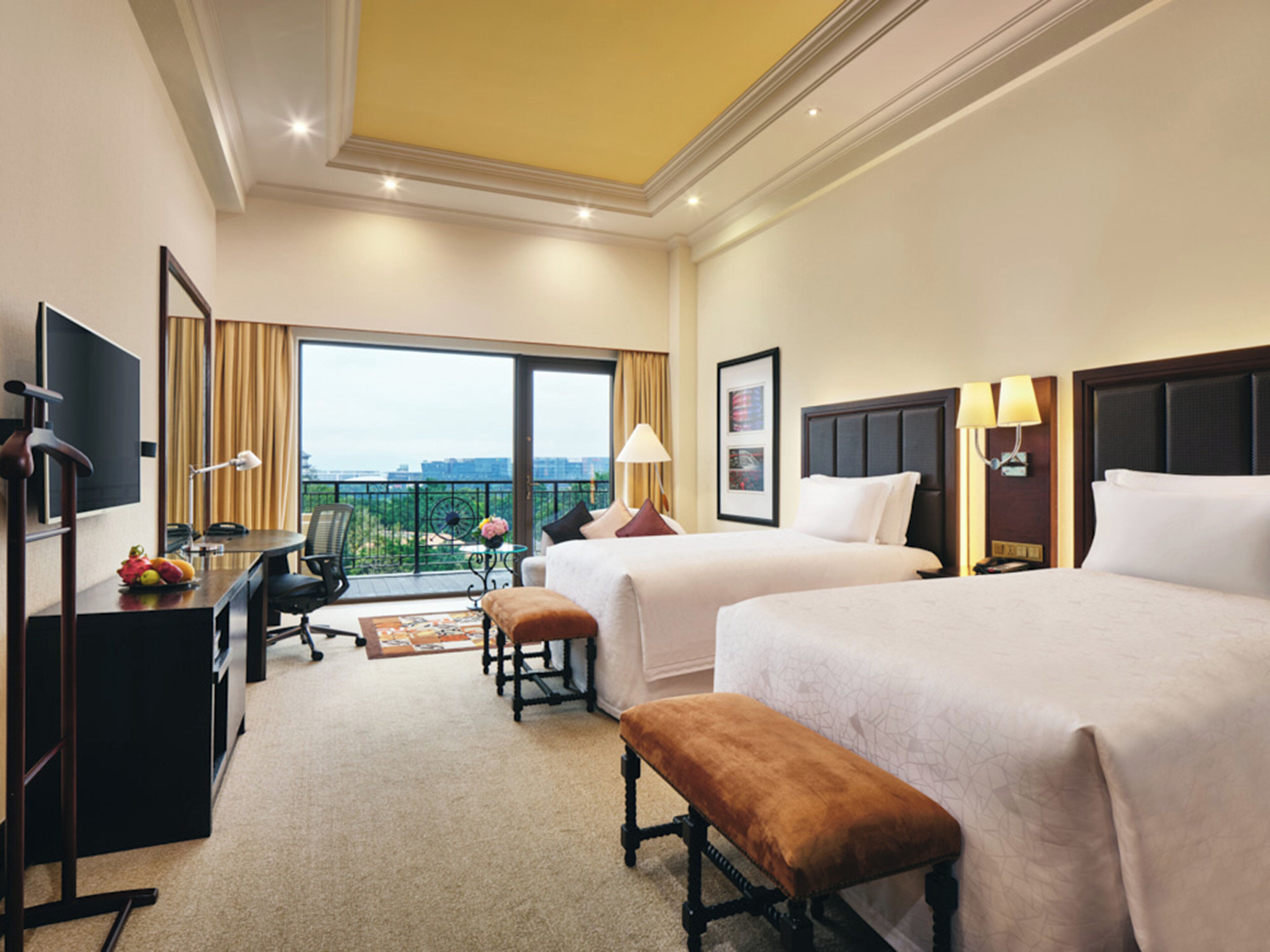 A hotel room with two beds, a desk, a chair, a TV, and a balcony with a view.