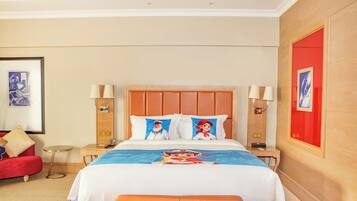 Una camera d'albergo con un letto grande, un divano rosso, un tavolino rotondo e due lampade ai comodini.