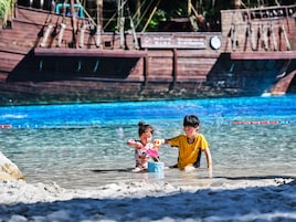 A sandy beach with clear blue water and a wooden boat structure in the background.