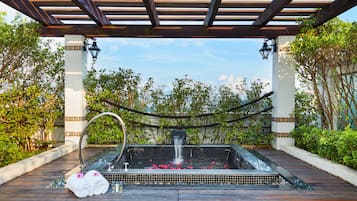 Zona de spa con hidromasaje, terraza de madera y vegetación circundante.