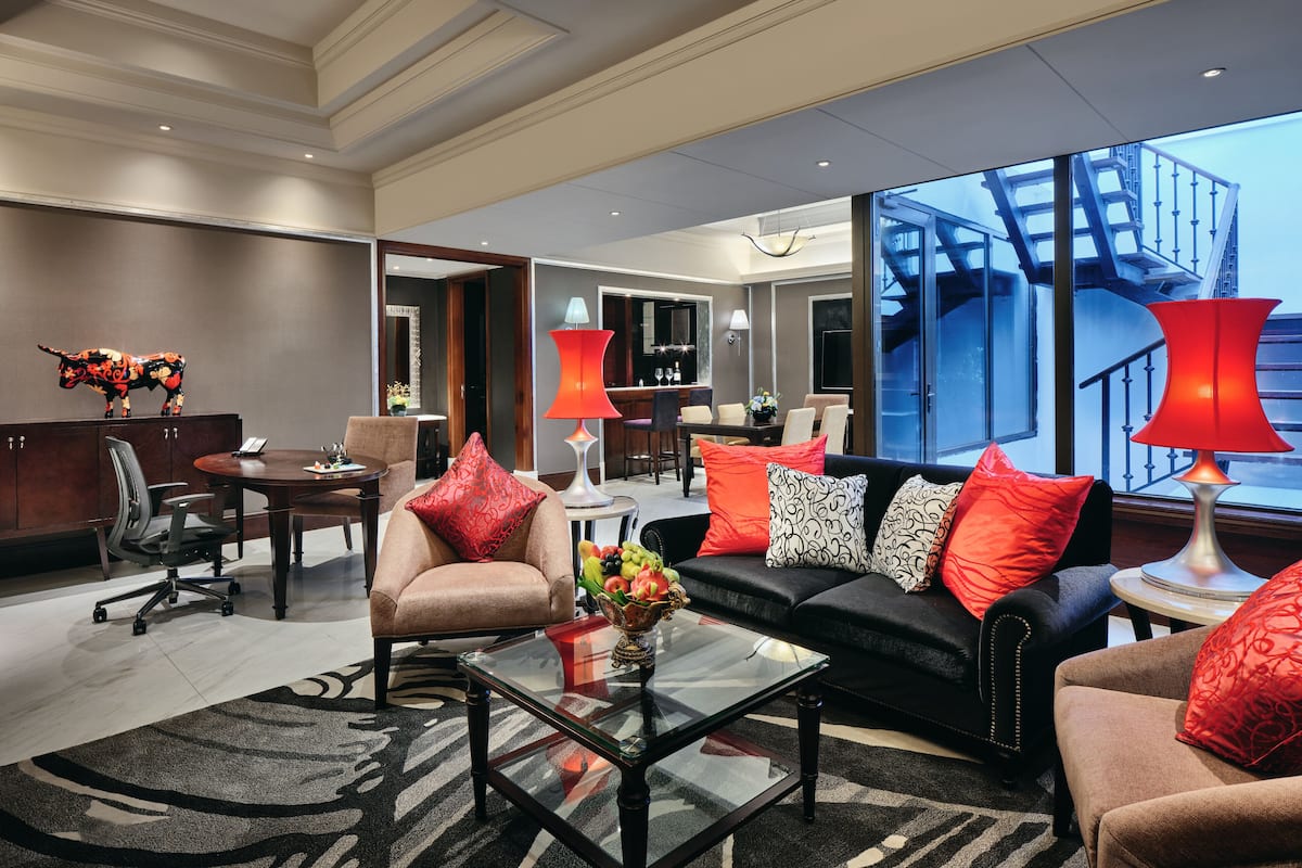 A modern hotel lobby with a seating area, a dining space, and a staircase leading to an upper level.