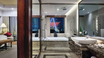 A modern bathroom with a large mirror, dual sinks, a bathtub, and a view of a cityscape at night.
