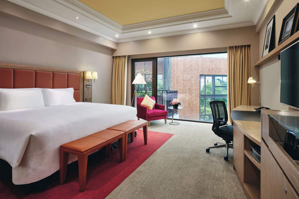 A hotel room with a large bed, a desk with a chair, a small table with a lamp, and a TV.