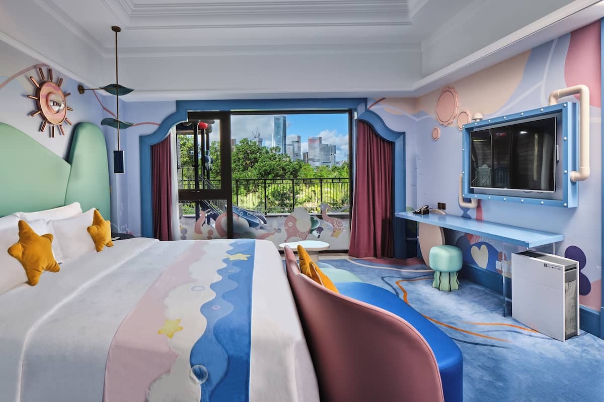 A modern hotel room with a large bed, a desk, and a city view.
