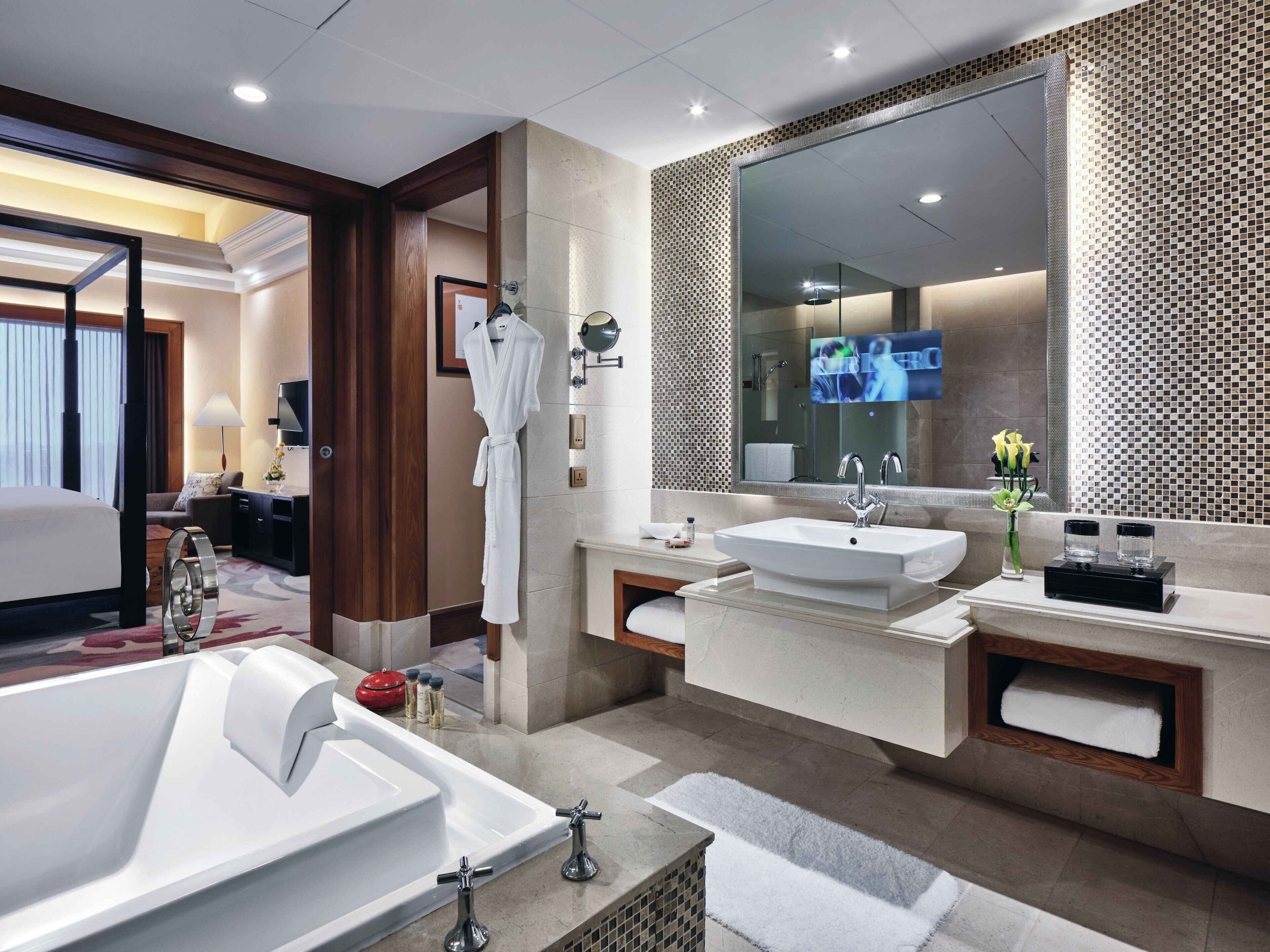 Une salle de bain d’hôtel moderne, dotée d’une grande baignoire, de deux lavabos, d’un miroir et d’un téléviseur.
