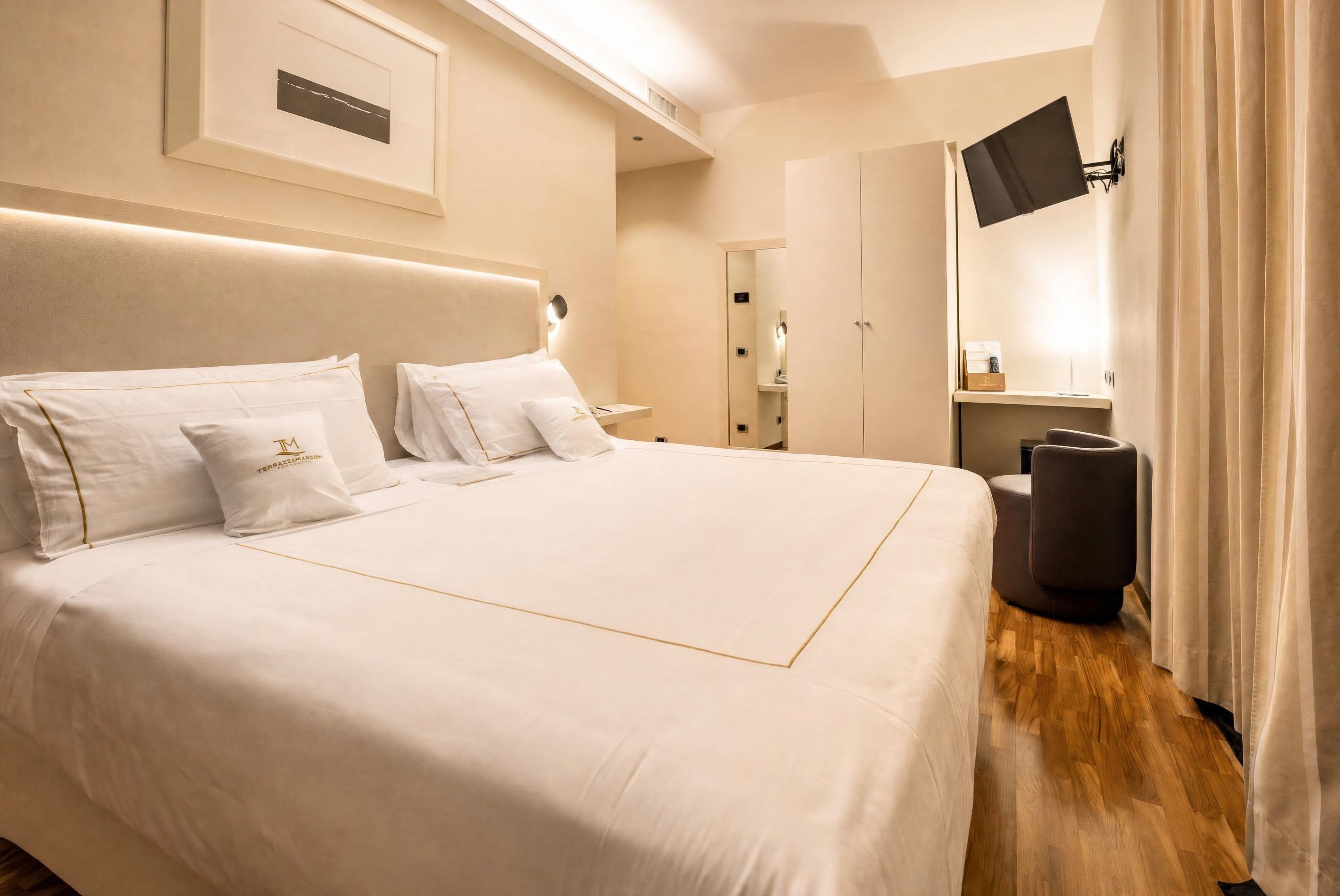 A hotel room with a large bed, a flat-screen TV mounted on the wall, a wardrobe, and a mirror.