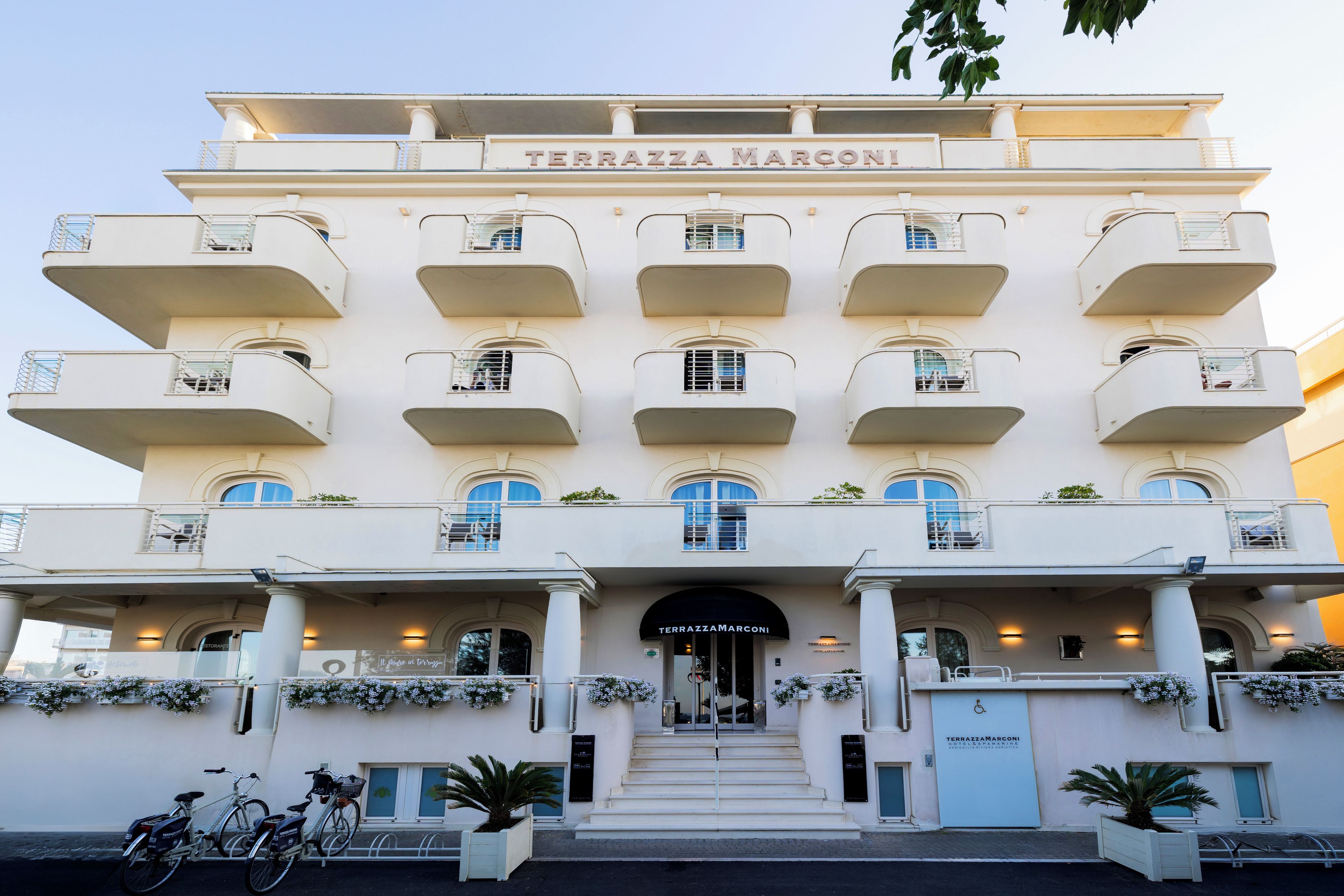 Un hotel de varios pisos con una entrada destacada, balcones y un letrero que dice 'TERRAZZA MARCONI'.